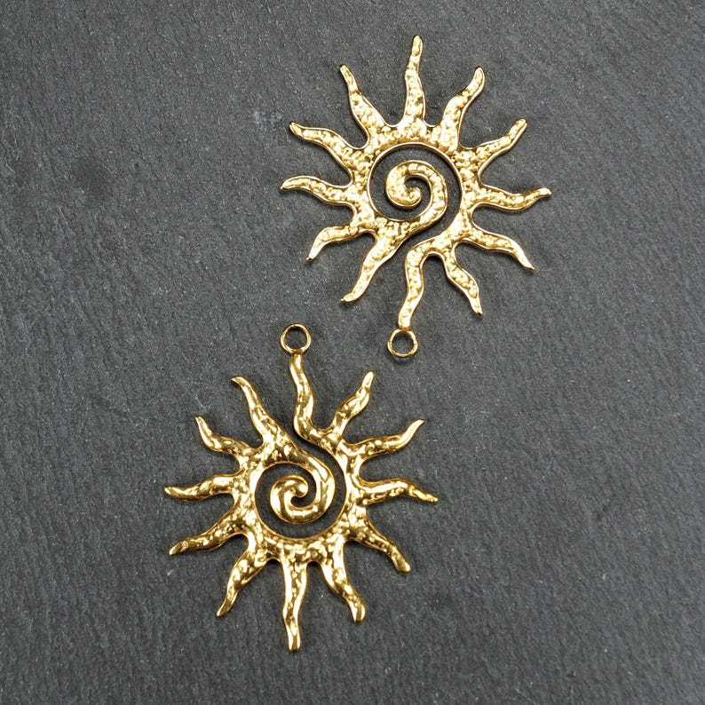 May include: Two gold-toned metal sunburst charms with a spiral design in the center. The charms have a hammered texture and are perfect for jewelry making.