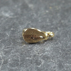 May include: A gold leaf charm with a detailed design. The charm has a loop on the back for attaching to jewellery or other crafts.