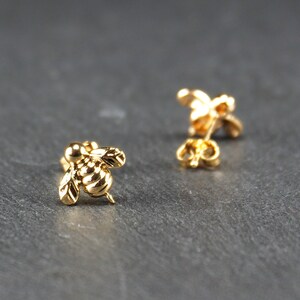 May include: A pair of gold bee stud earrings. The bee is detailed with wings and a textured body.