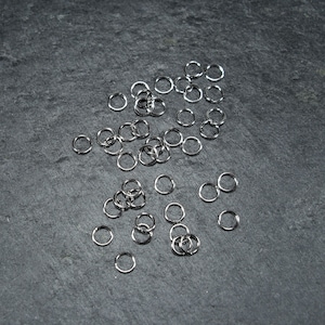 May include: A large quantity of silver jump rings, scattered on a dark grey surface.