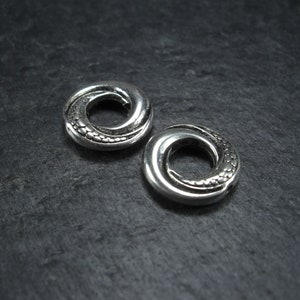 May include: Two silver metal rings with a twisted design and a textured surface. The rings are approximately 2.5 cm in diameter.