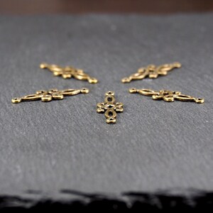 Puede incluir: Cinco adornos decorativos de metal dorado con dise&ntilde;os intrincados. Los adornos tienen forma de cruz y de rect&aacute;ngulo largo y estrecho.