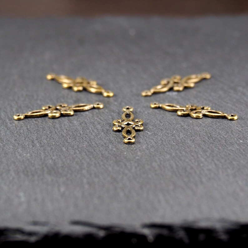 Puede incluir: Cinco adornos decorativos de metal dorado con dise&ntilde;os intrincados. Los adornos tienen forma de cruz y de rect&aacute;ngulo largo y estrecho.