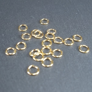 May include: A pile of gold jump rings, a type of jewellery finding, on a grey surface.
