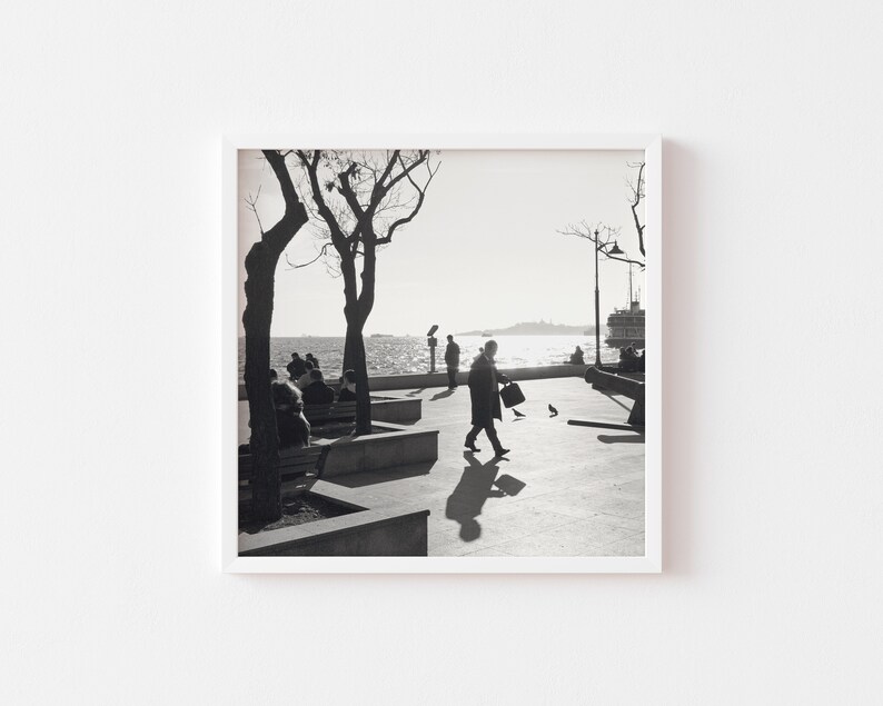 May include: Black and white photograph of people sitting on benches along a waterfront with a ferry in the distance.