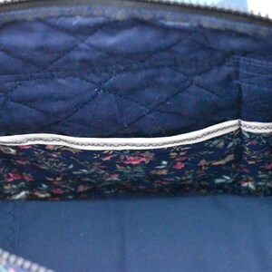 Op de afbeelding: Binnenaanzicht van een marineblauwe gewatteerde tas met een bloemenprintzak. De binnenkant van de tas heeft een ruitvormig stikselpatroon. De zak is gevoerd met een bloemenstof in roze, groene en blauwe tinten. De tas heeft een rits.