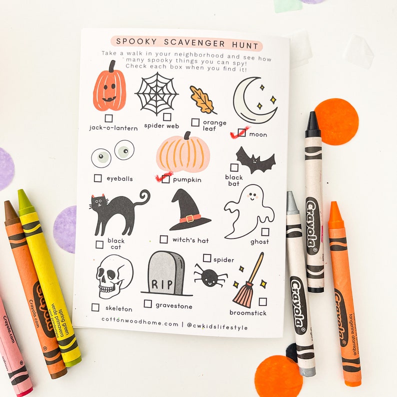May include: A white paper scavenger hunt sheet titled SPOOKY SCAVENGER HUNT with black and orange illustrations of Halloween items like a jack-o-lantern, spider web, moon, black cat, witch's hat, ghost, skull, gravestone, and broomstick, with crayons.
