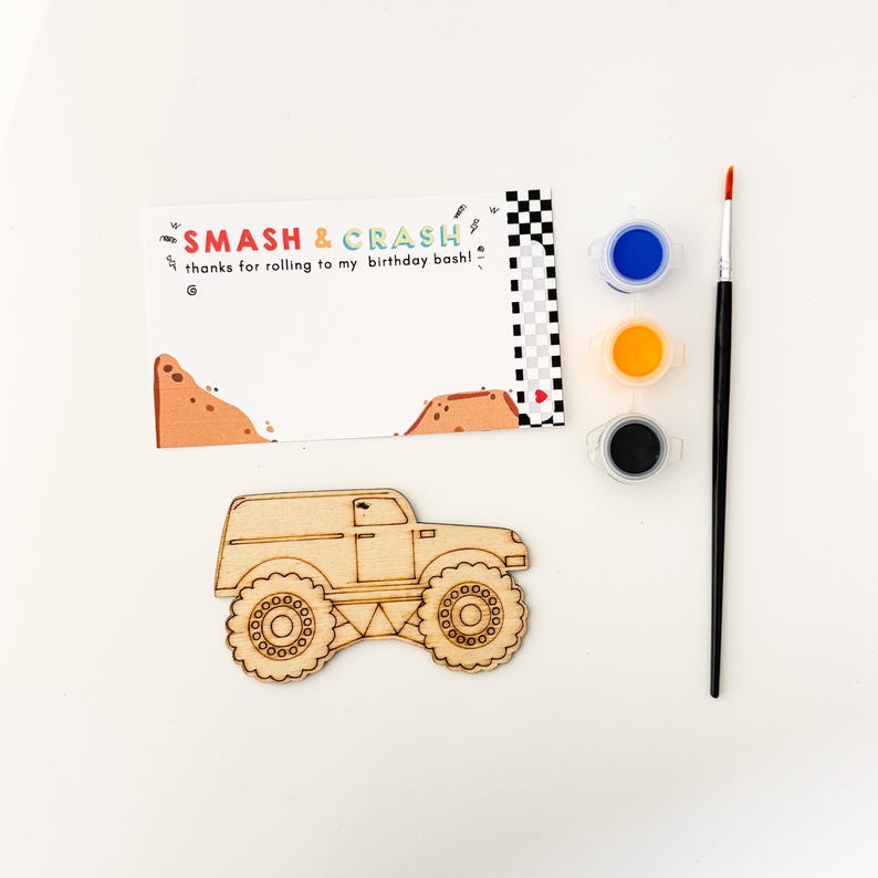May include: A wooden monster truck cutout with a blank surface for painting. The kit includes three small bottles of paint in blue, yellow, and black, and a paintbrush. The card reads "Smash & Crash" and "Thanks for rolling to my birthday bash!"