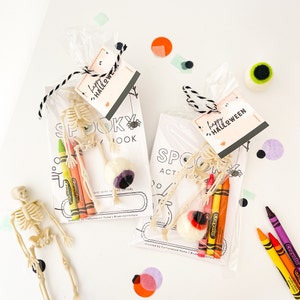 May include: Two clear plastic favor bags containing a Spooky Activity Book, a plastic skeleton, three Crayola crayons in yellow, orange, and red, and a felt eyeball. Each bag is tied with black and white twine and a Happy Halloween gift tag.