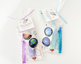 May include: Two clear cellophane bags filled with space-themed party favors. Each bag has a tag that reads "THANKS FOR MAKING MY BIRTHDAY A BLAST!" and includes stickers of planets and a bubble wand. One bag is tied with a purple ribbon, the other with blue.