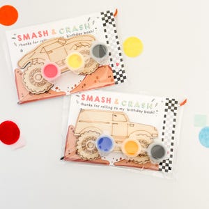 May include: Two clear plastic bags with wooden monster truck paint-your-own kits. Each kit includes a wooden monster truck, four small paint pots, and a card that says "Smash & Crash thanks for rolling to my birthday bash!"