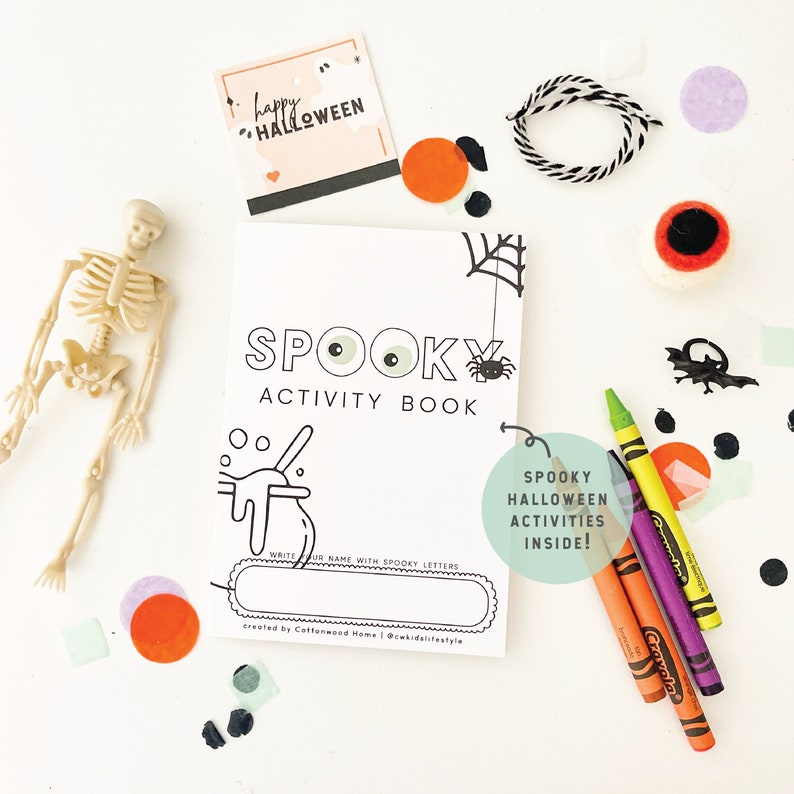 May include: A white Spooky Activity Book with black line art of a spider web, spider, and cauldron. The cover features the text Spooky Activity Book, a name line, and a green circle with the text Spooky Halloween Activities Inside. Includes a plastic skeleton, crayons, and Halloween-themed paper confetti.