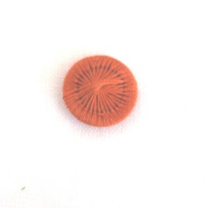 May include: A round, orange button with a woven design. The button is made of thread and has a raised centre.