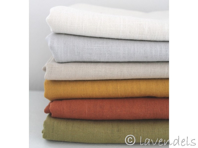 May include: Stack of five fabric swatches in different colors: white, light gray, beige, mustard yellow, and rust orange. The swatches are made of linen and have a textured surface.