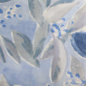 Peut inclure: Un tissu avec un motif floral de style aquarelle. Le design présente de grandes feuilles stylisées dans des tons de gris et de blanc, sur un fond bleu clair. De petits accents bleus ajoutent des détails, créant un aspect doux et artistique.