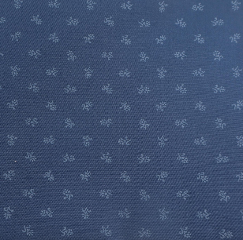 K&ouml;nnte beinhalten: Nahaufnahme eines blauen Stoffes mit einem sich wiederholenden Muster aus kleinen, hellblauen floralen Designs. Der Stoff hat eine subtile Textur, und das Blumenmuster ist gleichm&auml;&szlig;ig &uuml;ber die Oberfl&auml;che verteilt.