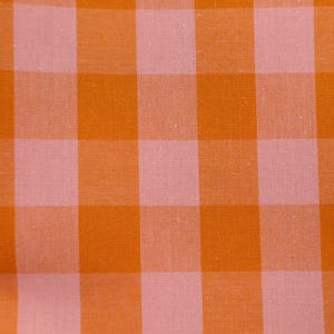 Könnte beinhalten: Nahaufnahme eines Stoffes mit einem großen orangefarbenen und hellrosa Vichy-Muster. Die Quadrate sind gleichmäßig groß und erzeugen ein klassisches, strukturiertes Design. Der Stoff scheint Baumwolle oder ein ähnliches Webmaterial zu sein.