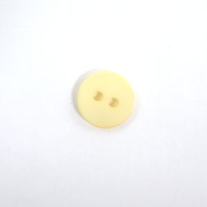 Peut inclure: Un bouton rond jaune pâle avec deux trous. Le bouton est fait d'un matériau lisse et solide sur un fond blanc. Convient aux projets de couture et à la réparation de vêtements. Le diamètre du bouton est d'environ 2 cm.