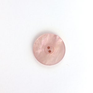 May include: A pink, two-hole button with a pearlescent finish.