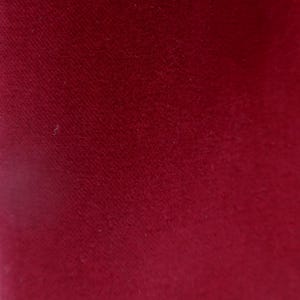 Op de afbeelding: Close-up van een effen rode stof met een subtiele textuur. Het materiaal lijkt zacht te zijn, mogelijk fluweel of vilt, met een lichte glans. De kleur is een diepe, rijke tint rood.
