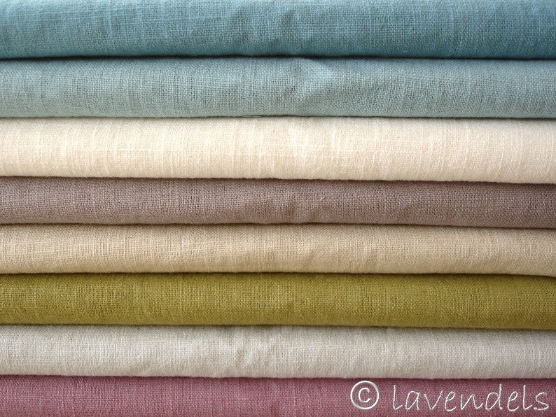May include: A stack of eight different colored linen fabrics. The fabrics are folded neatly and arranged in a graduated color scheme, starting with a light blue and ending with a deep pink.