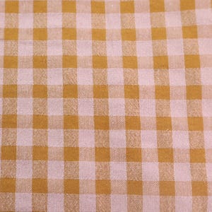 Op de afbeelding: Close-up van een stof met een ruitpatroon. Het patroon heeft een herhalend raster van vierkanten in licht mosterdgeel en lichtroze. De stof heeft een licht getextureerd uiterlijk.