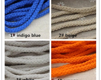 May include: Close-up of four sections of rope in different colors: indigo blue, beige, white, and orange. Each section has a label with a number and color name. The ropes are tightly coiled and have a textured appearance.
