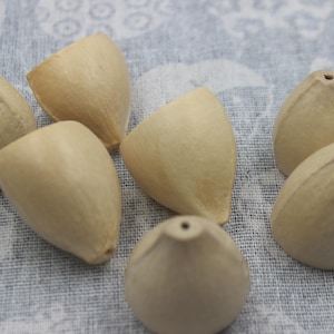Peut inclure: Un ensemble de six perles en bois de couleur beige clair, en forme de goutte d'eau. Chaque perle présente une finition mate et lisse avec un petit trou central au sommet, conçu pour l'enfilage. Les perles ont un aspect naturel et organique.