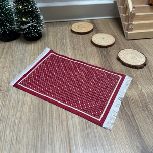 Könnte beinhalten: Ein kleiner roter Teppich mit weißem Rand und einem weißen und roten Muster. Der Teppich hat einen Fransenrand.