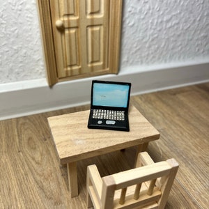 Könnte beinhalten: Ein Miniatur-Tisch- und Stuhlset aus Holz mit einem schwarzen Laptop auf dem Tisch. Das Set ist aus hellbraunem Holz gefertigt und perfekt für ein Puppenhaus oder eine Miniatur-Szene.