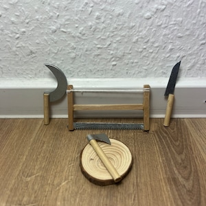 Może przedstawiać: Miniaturowa drewniana piła, siekiera i sierp z drewnianymi uchwytami na drewnianej powierzchni. Narzędzia są ułożone na drewnianym plastrze.
