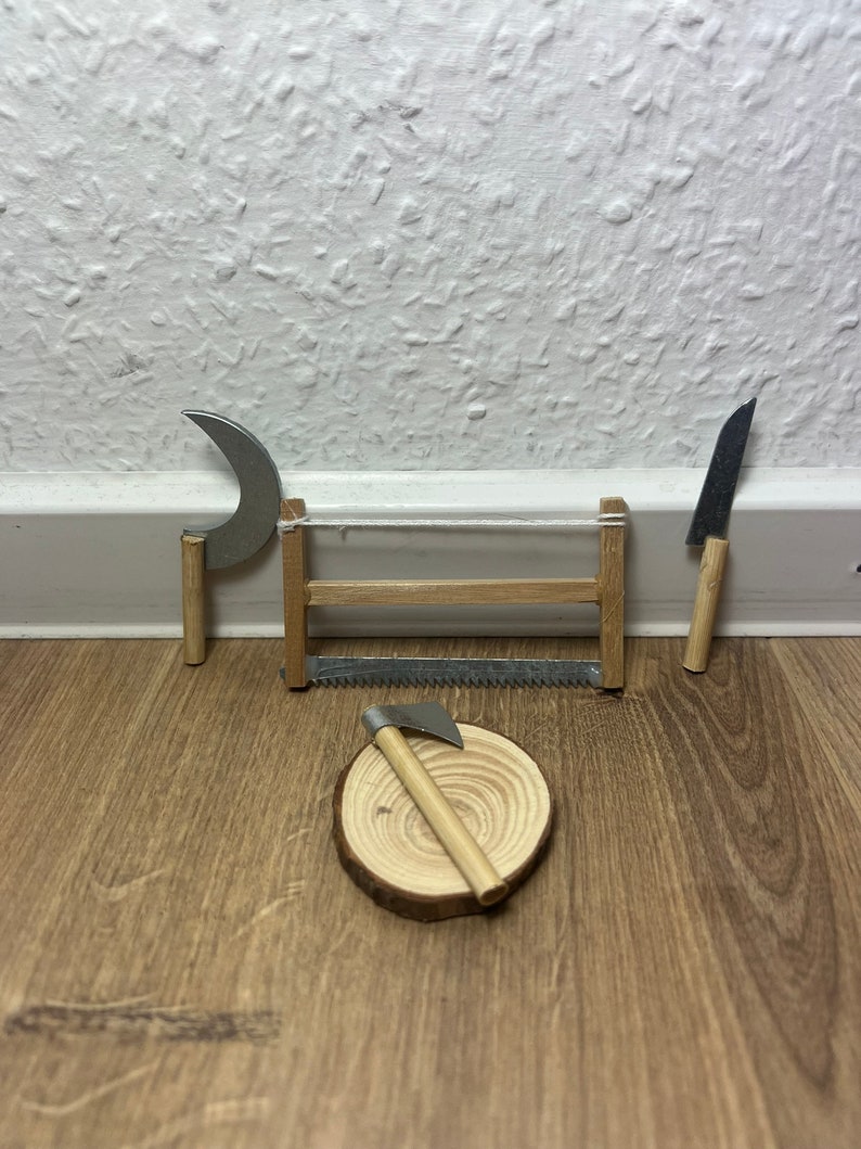 Może przedstawiać: Miniaturowa drewniana piła, siekiera i sierp z drewnianymi uchwytami na drewnianej powierzchni. Narzędzia są ułożone na drewnianym plastrze.