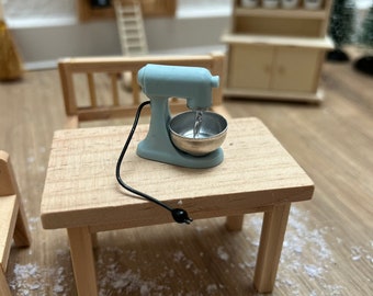 May include: A miniature blue stand mixer with a silver bowl on a wooden table. The mixer has a black cord.