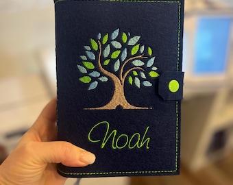 May include: A dark navy blue felt notebook cover featuring an embroidered tree with brown trunk and green and light blue leaves. The name Noah is embroidered in bright green cursive script below the tree. A lime green snap button secures the cover.