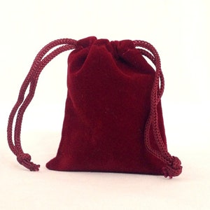 May include: A small, red velvet drawstring bag with a gathered top. The bag is made of soft, plush velvet and has a smooth, silky texture.