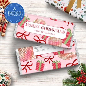 Peut inclure: Deux emballages de barres chocolatées roses sur le thème de Noël. Les emballages présentent le texte "Merry Christmas" et "The Williams" dans une bannière blanche. Le design comprend des boîtes cadeaux, des boules disco et des nœuds rouges.