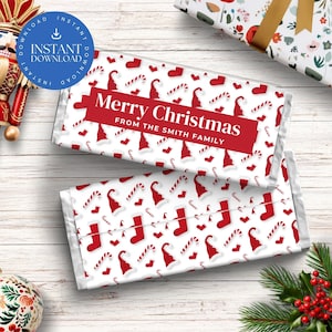 Può includere: Due confezioni di barrette di cioccolato con un design natalizio festivo. Le confezioni presentano un motivo di cappelli di Babbo Natale rossi, calze, bastoncini di zucchero e cuori su sfondo bianco. Il testo "Merry Christmas From The Smith Family" è visualizzato in un banner rosso.