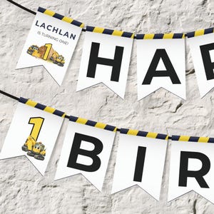 Könnte beinhalten: Eine Girlande mit weißen Wimpeln, die mit schwarzer Schnur verbunden sind. Die Wimpelbuchstaben bilden "HAPPY BIRTHDAY". Zusätzliche Wimpel zeigen den Namen "LACHLAN" und den Satz "IS TURNING ONE!" mit Baustellenfahrzeuggrafiken.
