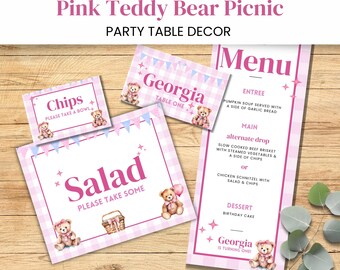 May include: Pink and white gingham table decorations for a teddy bear themed party. The decorations include a menu, table number sign, and signs for chips and salad. The menu includes the text "Georgia is turning one!"