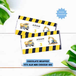 May include: Two printable chocolate bar wrappers featuring a yellow dump truck and excavator on a black and yellow striped background. The text "ADAM IS TURNING 3" is on each wrapper. The wrappers are designed to fit Aldi mini chocolate bars.