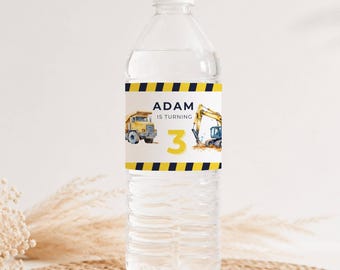 May include: A clear plastic water bottle with a custom label featuring a yellow dump truck, a yellow excavator, and the text ADAM IS TURNING 3. The label has black and yellow diagonal hazard stripes along the top and bottom edges.