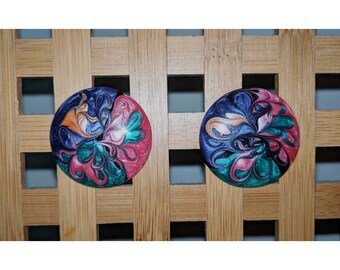 May include: A pair of round, colorful earrings with a swirling, abstract design. The earrings are made of resin and have a glossy finish. The colors are pink, blue, green, black, and orange.