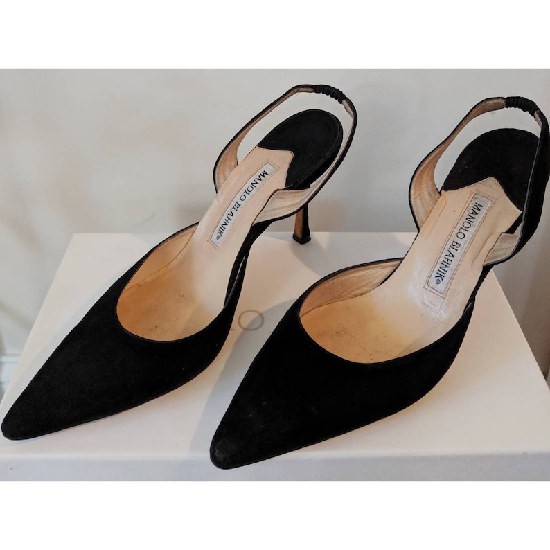 May include: A pair of black suede Manolo Blahnik slingback heels with a pointed toe and a thin stiletto heel.