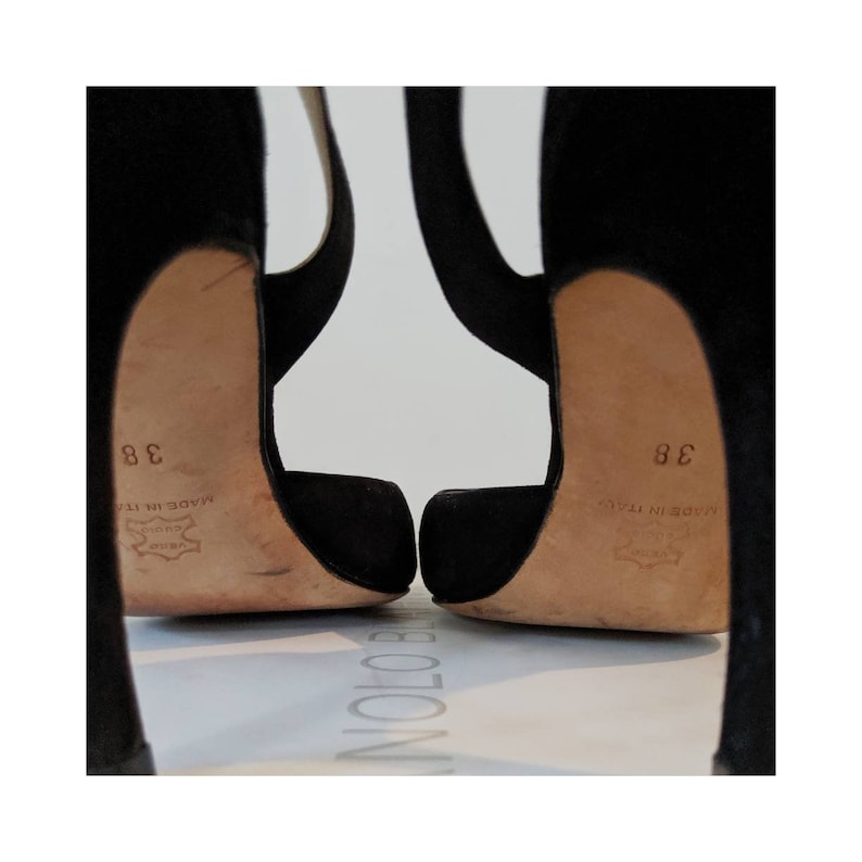 May include: A pair of black suede high heels with a pointed toe and a thin strap across the foot. The heels are approximately 4 inches tall and the shoes are size 38. The shoes are made in Italy.