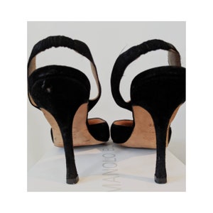 May include: A pair of black suede heeled shoes with a slingback design. The shoes have a pointed toe and a high stiletto heel.