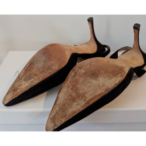 May include: A pair of black suede heeled shoes with pointed toes and a slingback design. The shoes are shown from the bottom, revealing the leather soles.