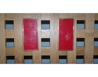 May include: Two red rectangular cabinet knobs with gold trim, mounted on a wooden surface.