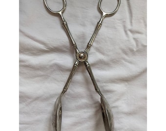 May include: Silver salad tongs with a bamboo-style design. The tongs have a rounded, spoon-like shape at the ends.