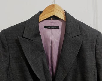 May include: A dark gray blazer with a pink lining and a black label that reads "Elie Tahari" hanging on a wooden hanger.