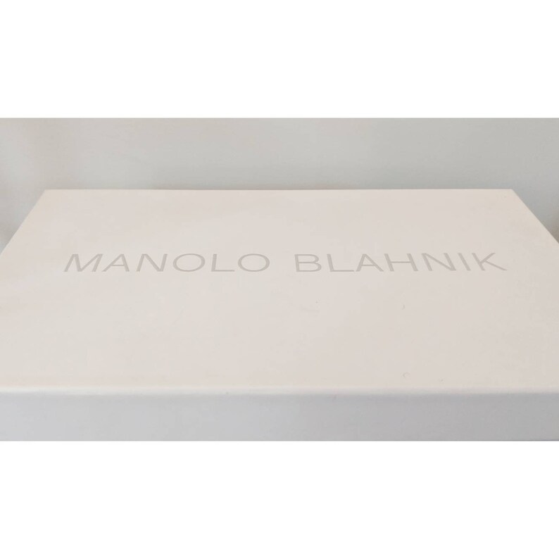 May include: A white box with the text "MANOLO BLAHNIK" printed in gray on the top.